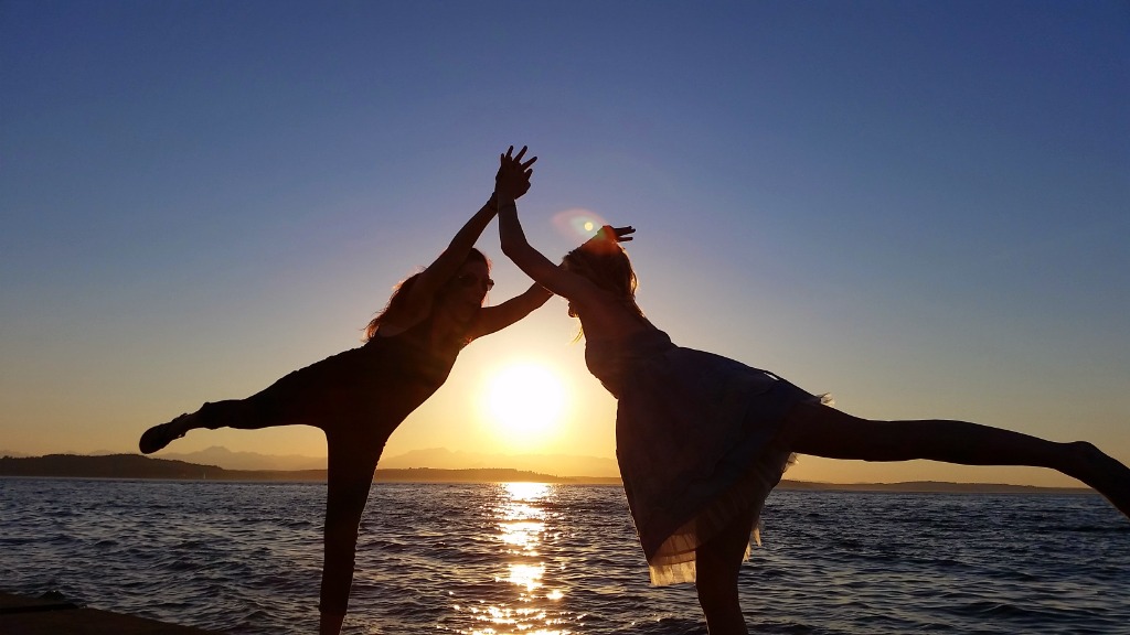 Two young people silhouetted against a beautiful sunset over the water